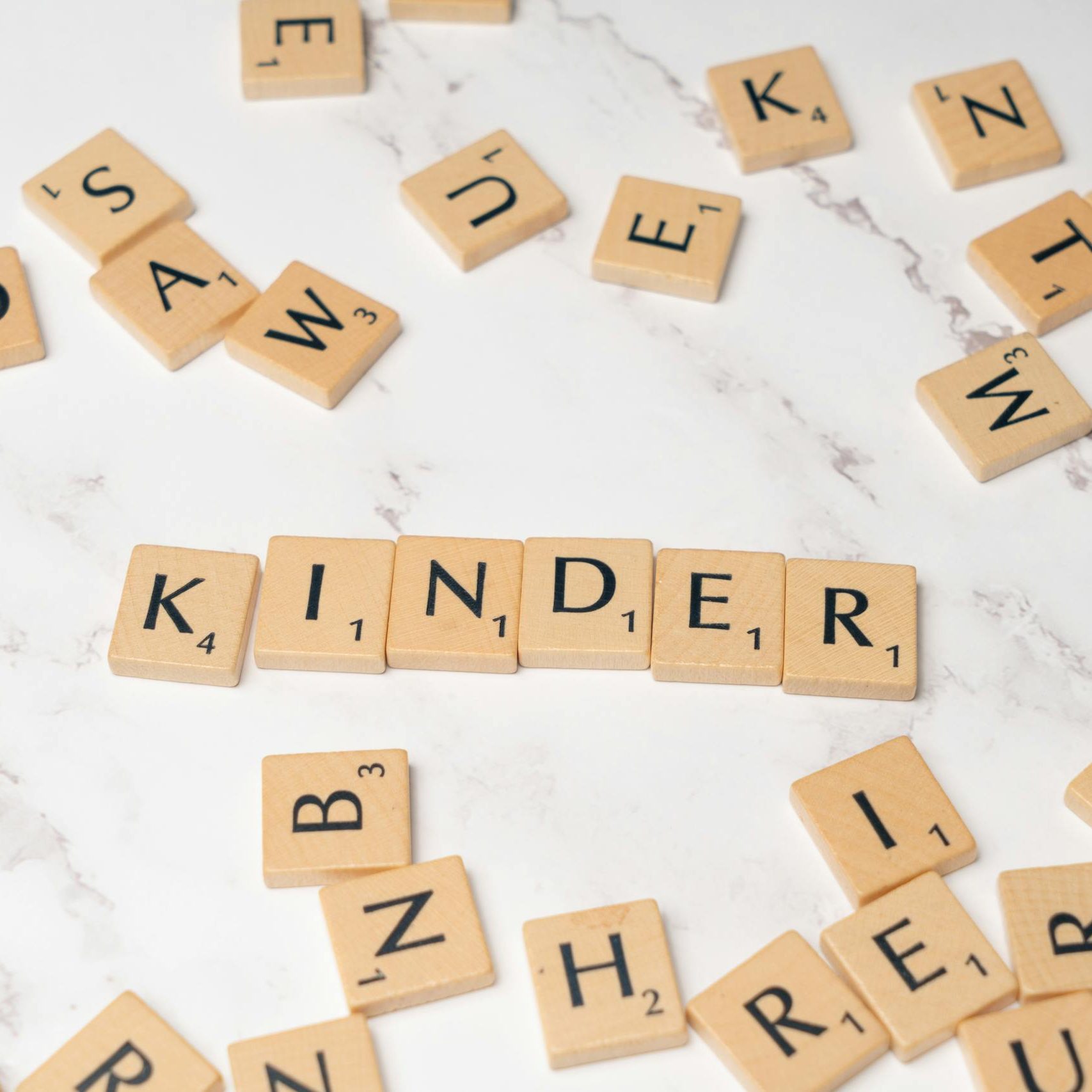 Scrabble tiles spelling 'Kinder' on a marble background, ideal for educational content.